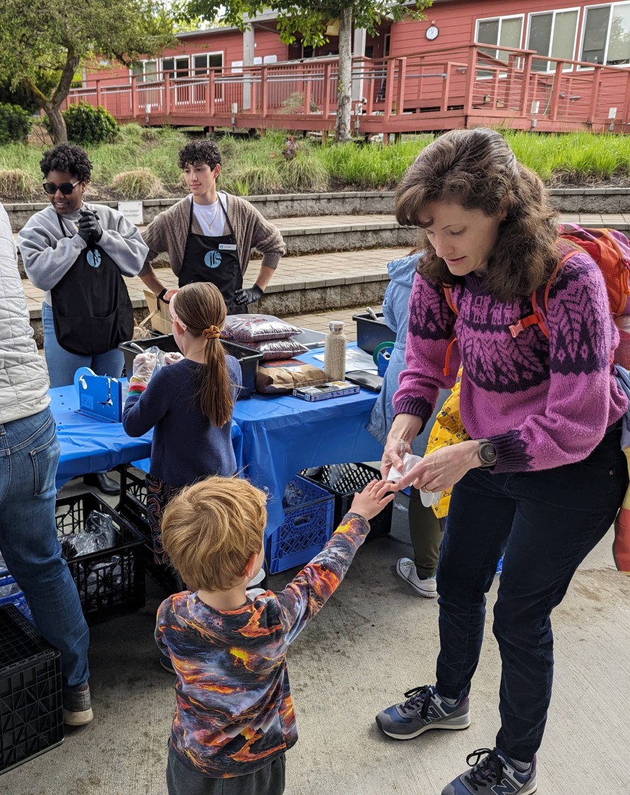 Little kid handing a woman something as two teenagers help at a volunteer event