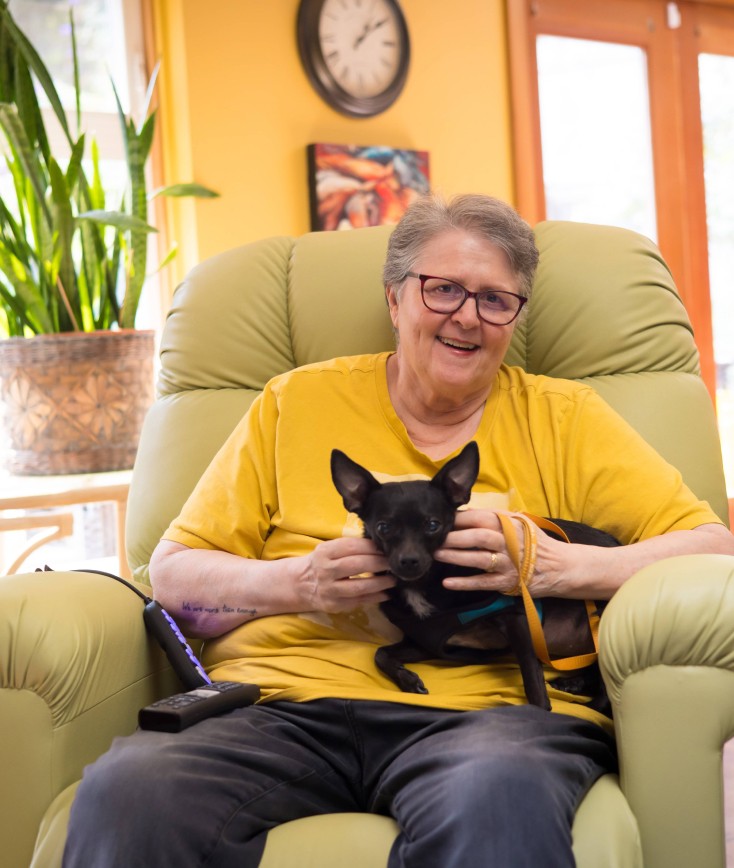 Woman sitting in a lounge chair holding a little black dog