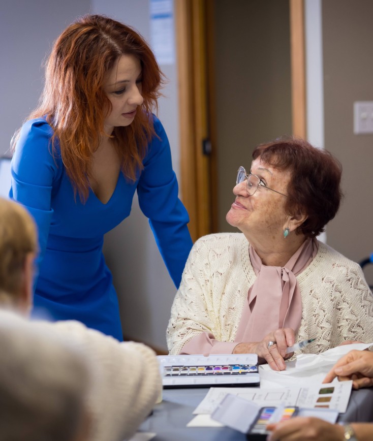 Woman in blue helping an older women sitting down with some paperwork