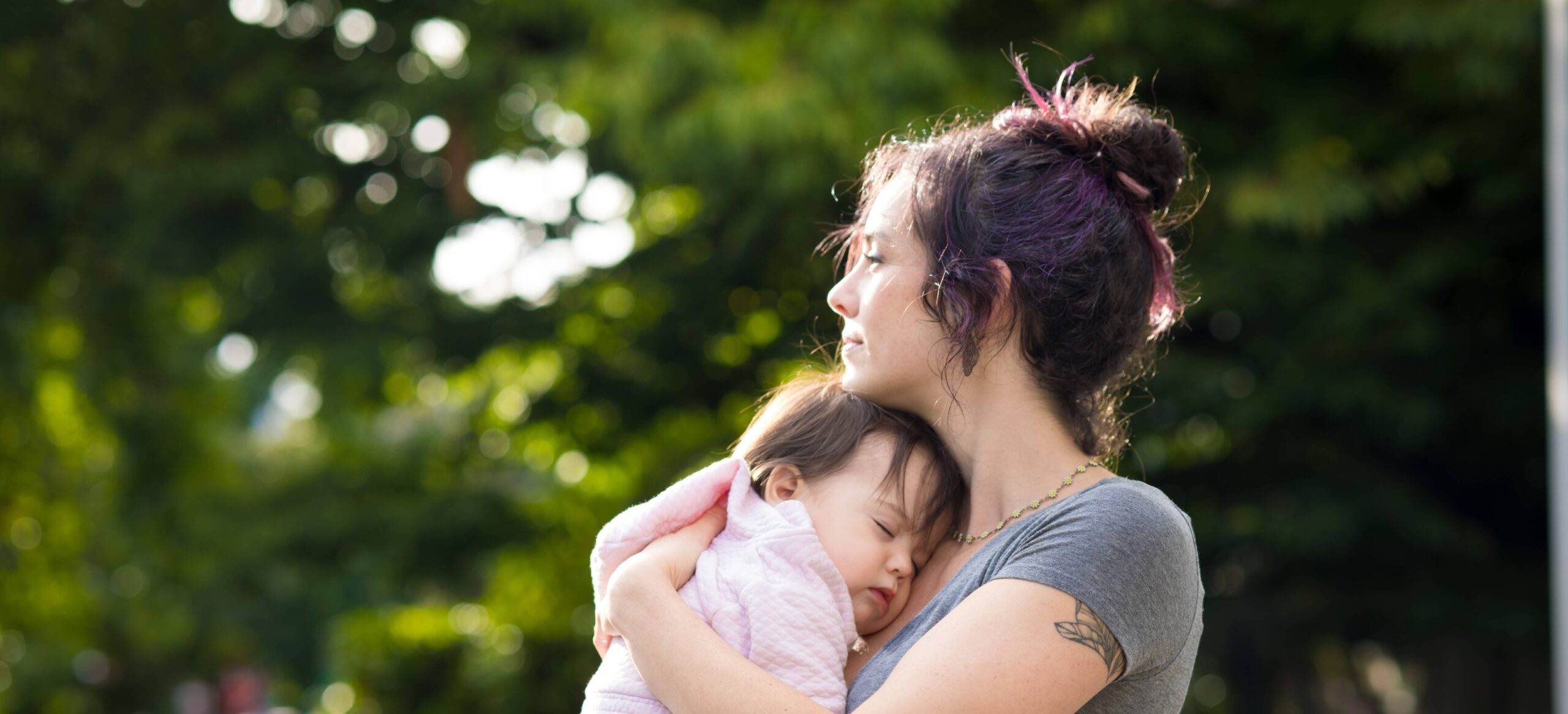 Woman holding her sleeping daughter as she looks off into the distance