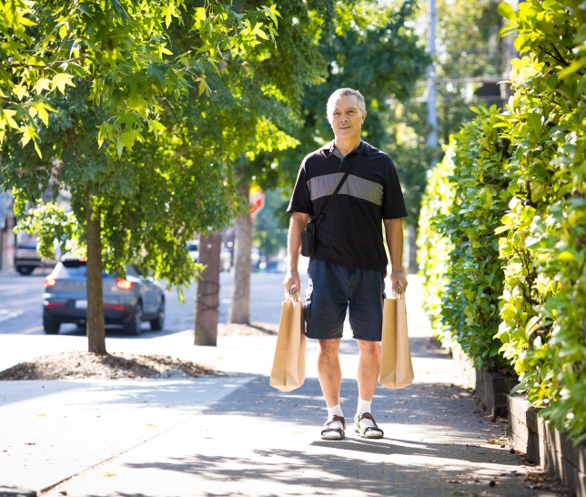 Man walking on the side-walk with two bags of food in hand