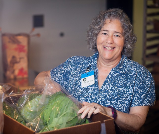 Woman volunteer for Polack Food Bank smiling at camera with crate of veggies in front of her