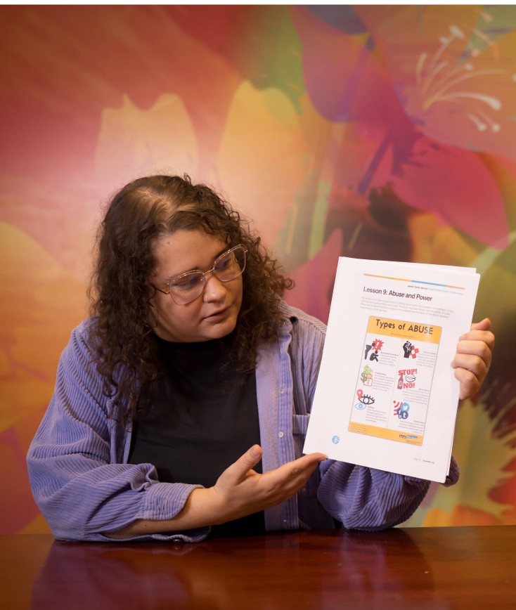 Woman sitting down at a conference table holding and looking at a paper on Abuse and Power in a room