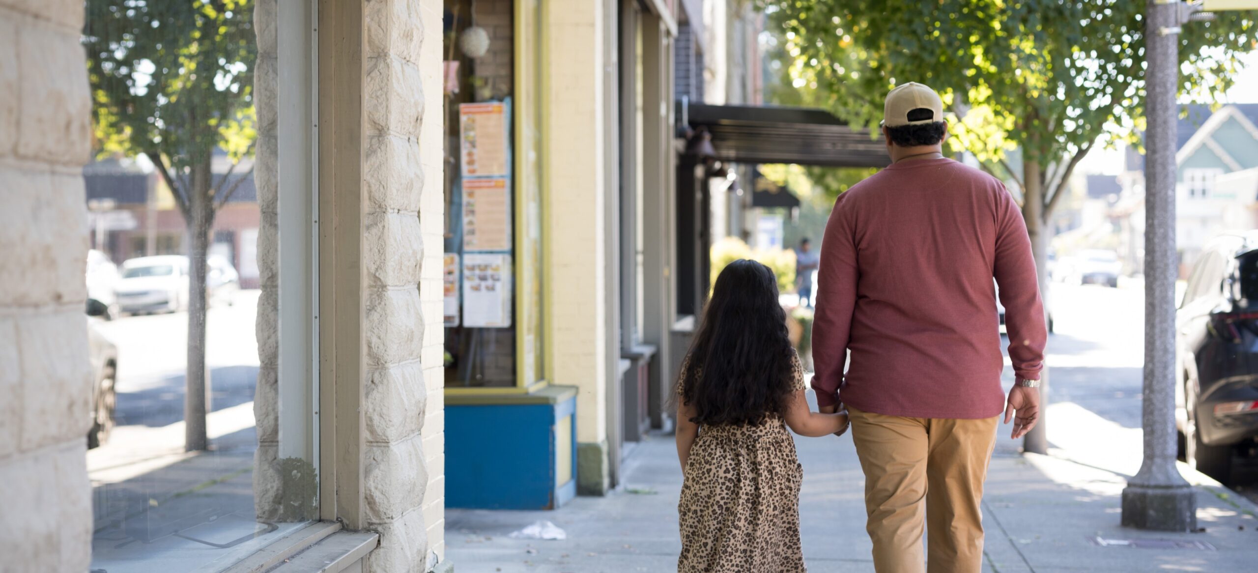 Father and daughter walking on the sidewalk next to some shops