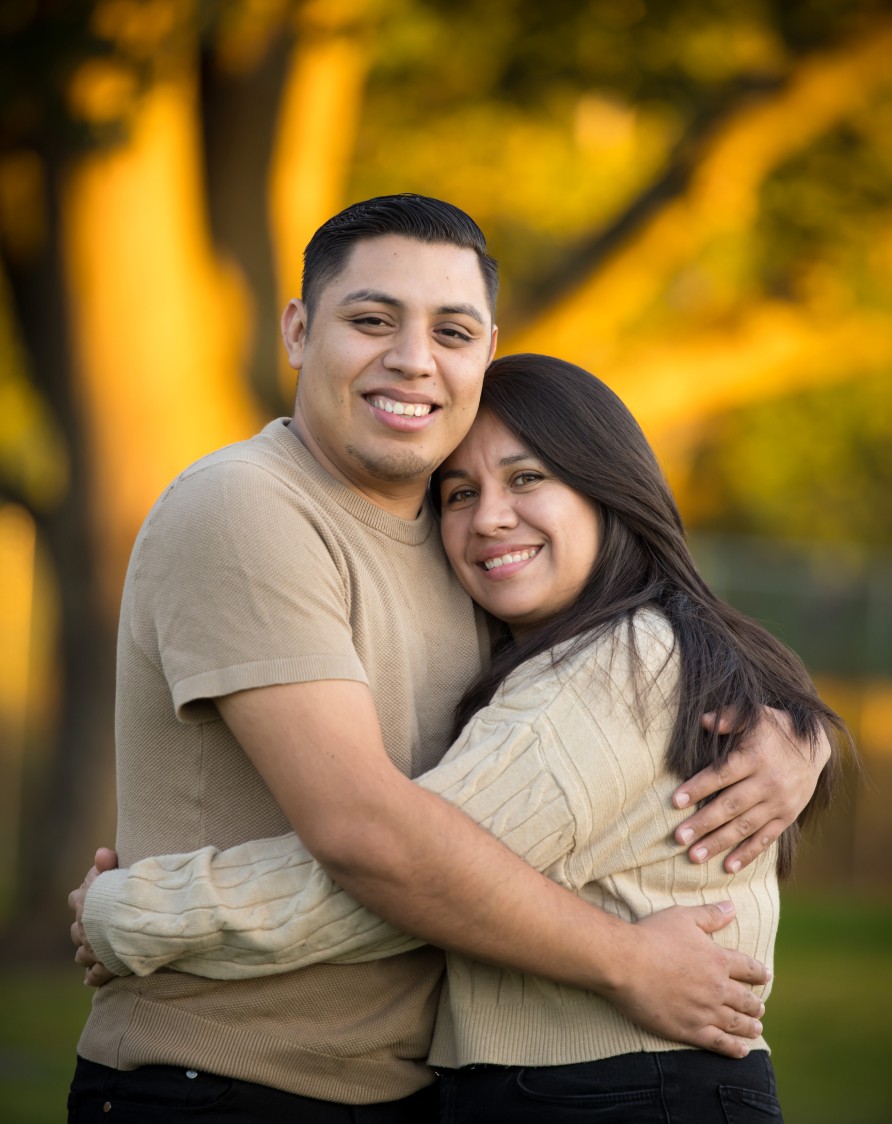 A couple hugging in a field as they look at the camera