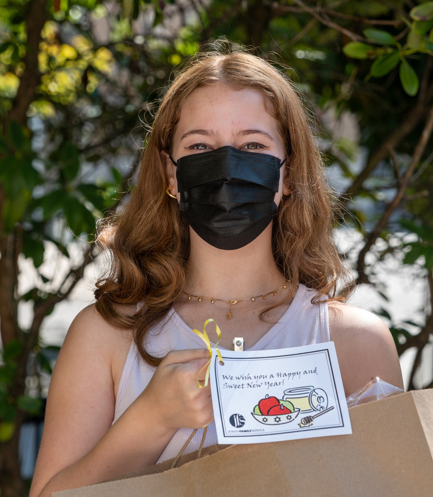 Teenage girl wearing a mask holding packaged grocery bag in had