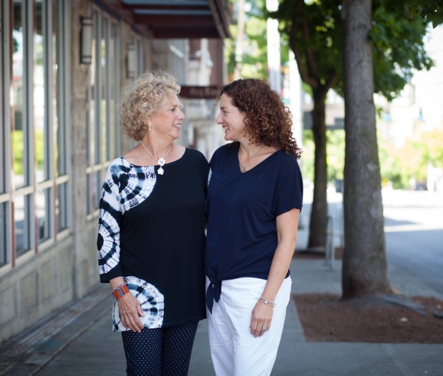 Two women side hugging while looking at one another on the sidewalk