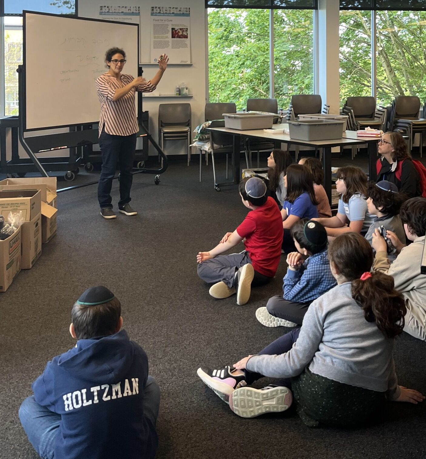 Rabbi Ronit standing in front of a group of kids sitting on the floor