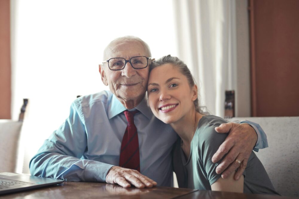 Older man with his arm around a smiling younger woman
