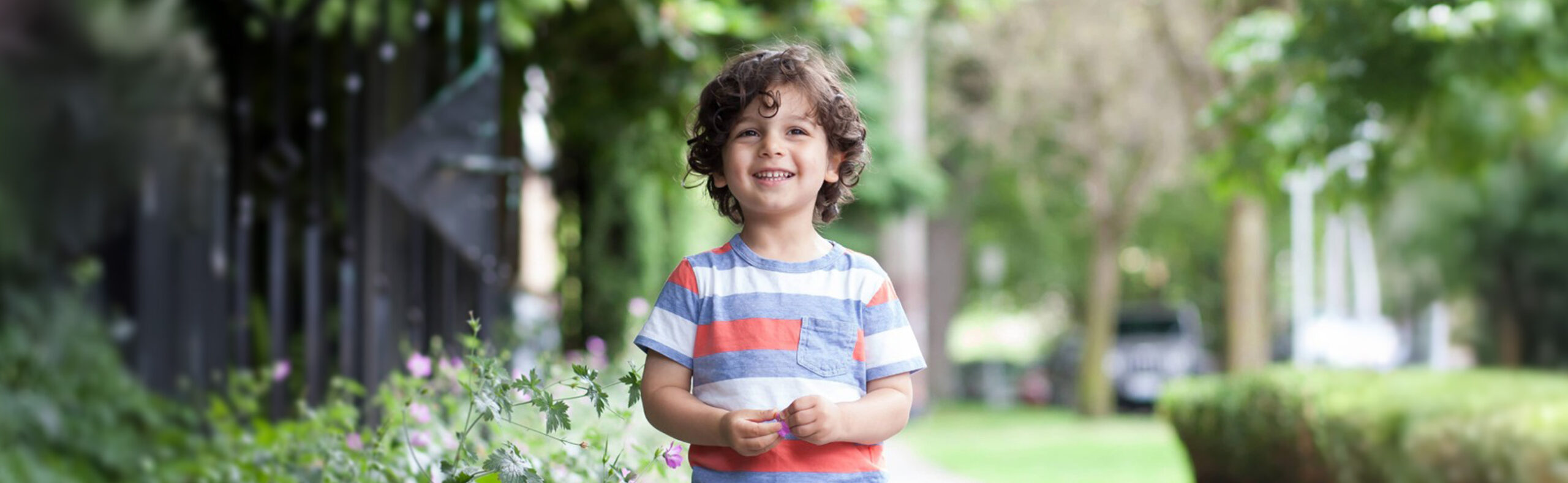 young boy smiling along a hedge of flowers