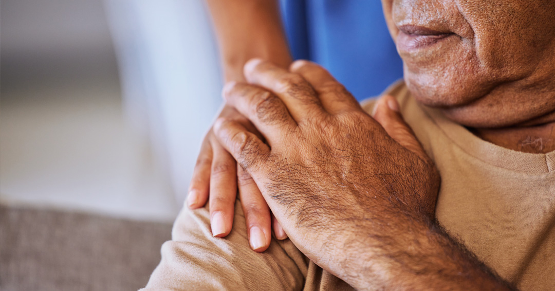 older adult with someone's hand on their shoulder